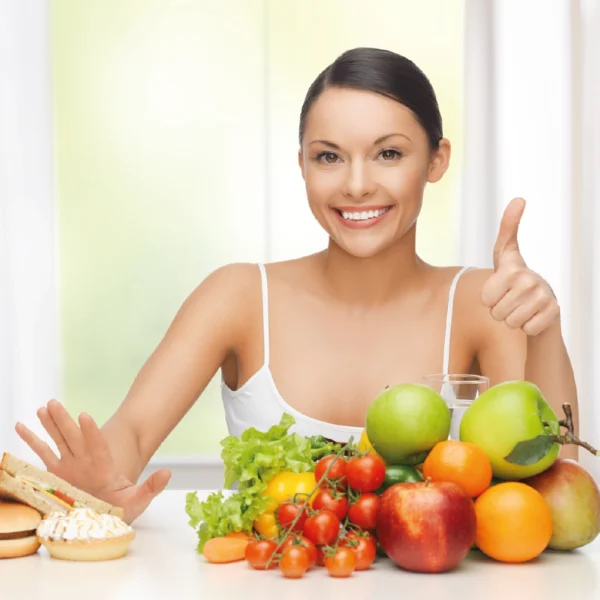 Mujer joven sonriendo y frutas al frente | Alimentación saludable clave para un bienestar sostenible | Alimentos Sostenibles
